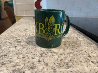 A green coffee mug sitting on top of a counter.|A green banner with the words " unborg " written in yellow.|A green mug with the logo of lord nelson.