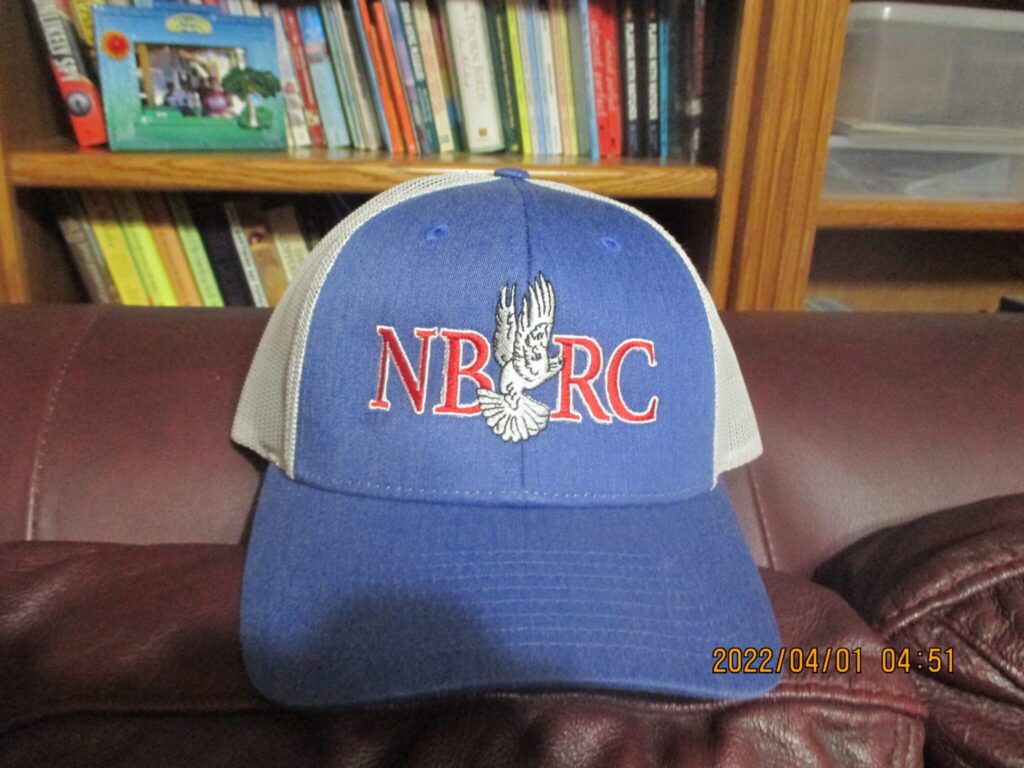 A blue and white baseball cap sitting on top of a brown couch.|A white hat sitting on top of a brown table.