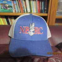 A blue and white baseball cap sitting on top of a brown couch.|A white hat sitting on top of a brown table.