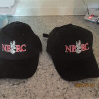 Two black hats are sitting on a counter.|A black hat with the words " i bird fly ".