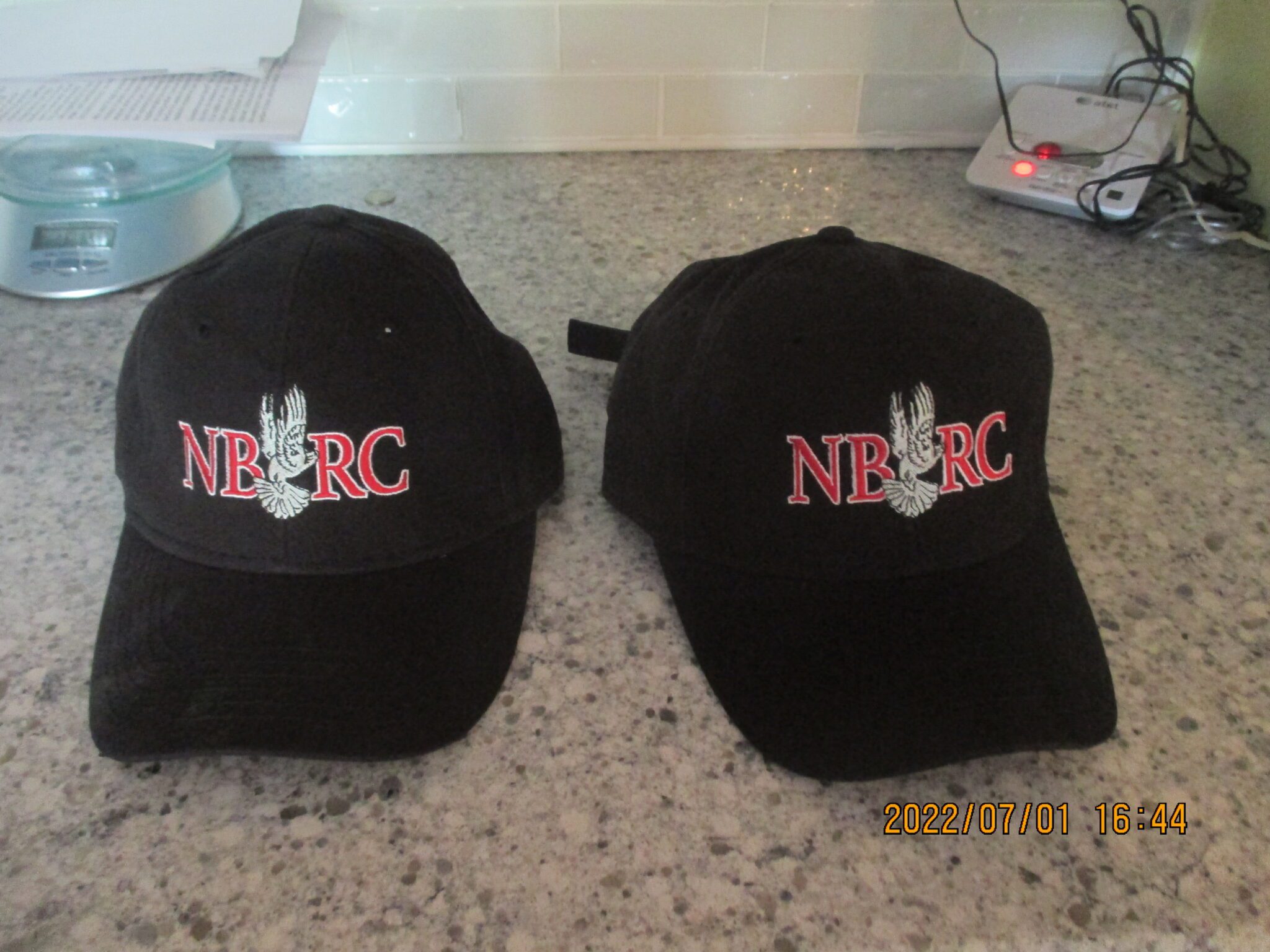 Two black hats are sitting on a counter.|A black hat with the words " i bird fly ".